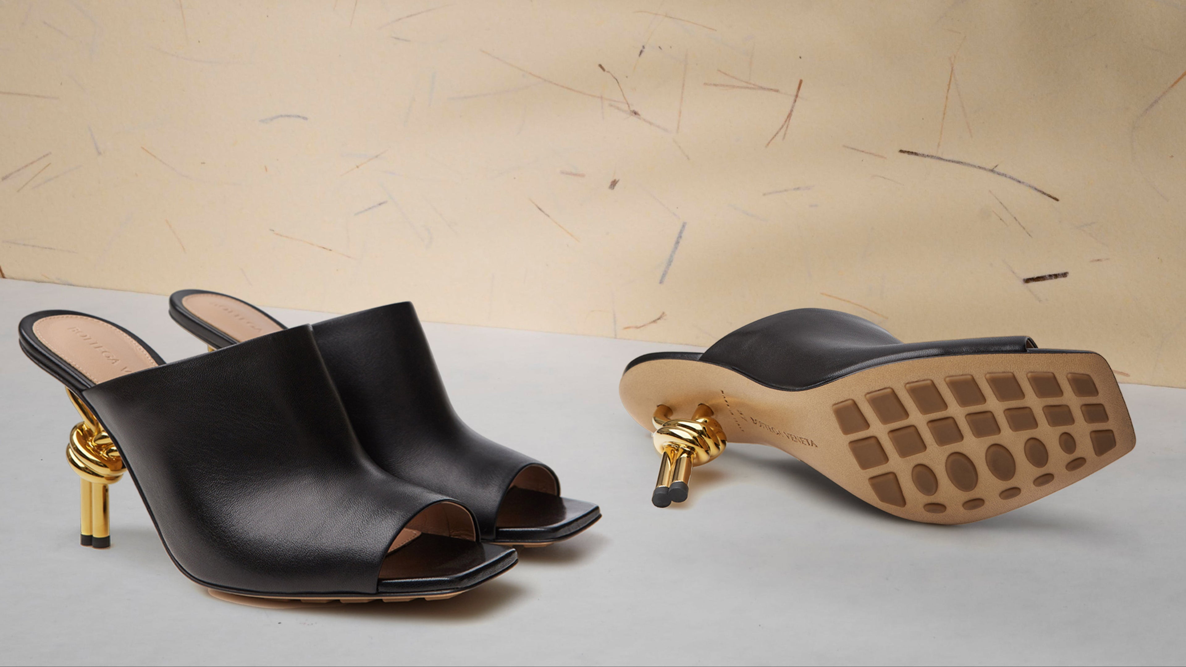 Black open-toe high-heeled shoes with gold accents on a light background